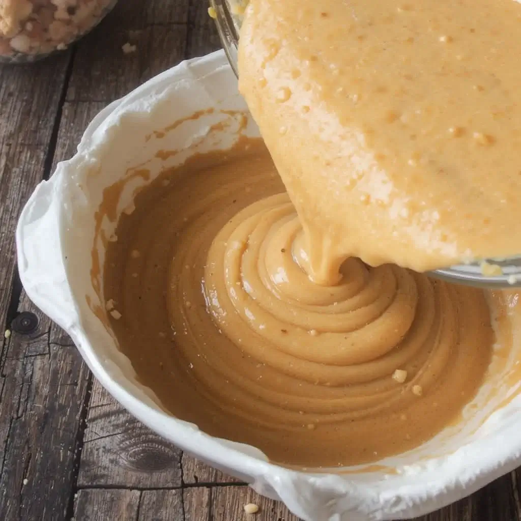 A bowl of smooth, creamy batter being poured to prepare Jamaican Sweet Potato Pudding, a beloved treat in Jamaican desserts, with a rich golden-brown color and a rustic wooden background.